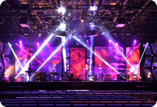 Un escenario luce espectacular con reflectores, escenografía, instrumentos musicales y luces de distintos colores. 