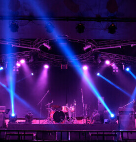 Imagen de un escenario con reflectores y luces. En medio se ven los instrumentos de una banda. 