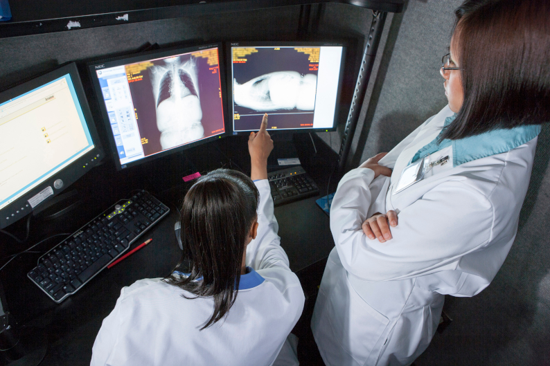 Un par de doctoras analizan radiografías desde un equipo con distintos monitores. 