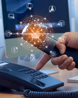 La mano de un oficinista marca un Teléfono IP. Del auricular surgen iconos digitales que representan email, dispositivos móviles y otros elementos que aportan mayores posibilidades a la comunicación moderna.  
