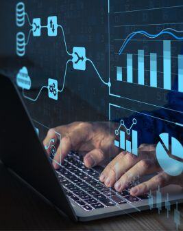 Las manos de un colaborador teclean en una laptop. Arriba aparecen símbolos digitales que representan gráficas y estadísticas de un reporte. 