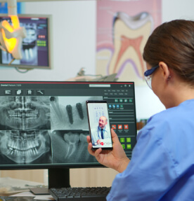Imagen de 2 médicos analizando una tomografía a distancia, por medio de una computadora y un teléfono móvil. 