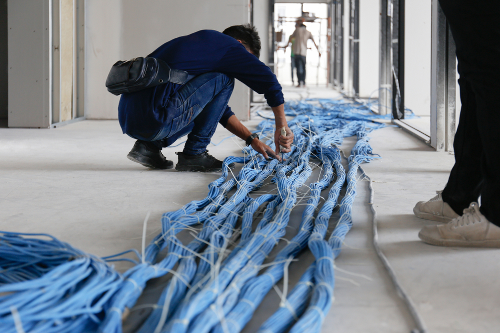 Un técnico agachado en el piso organiza un cableado de Fibra Óptica para mantenerlo ordenado en una instalación. 