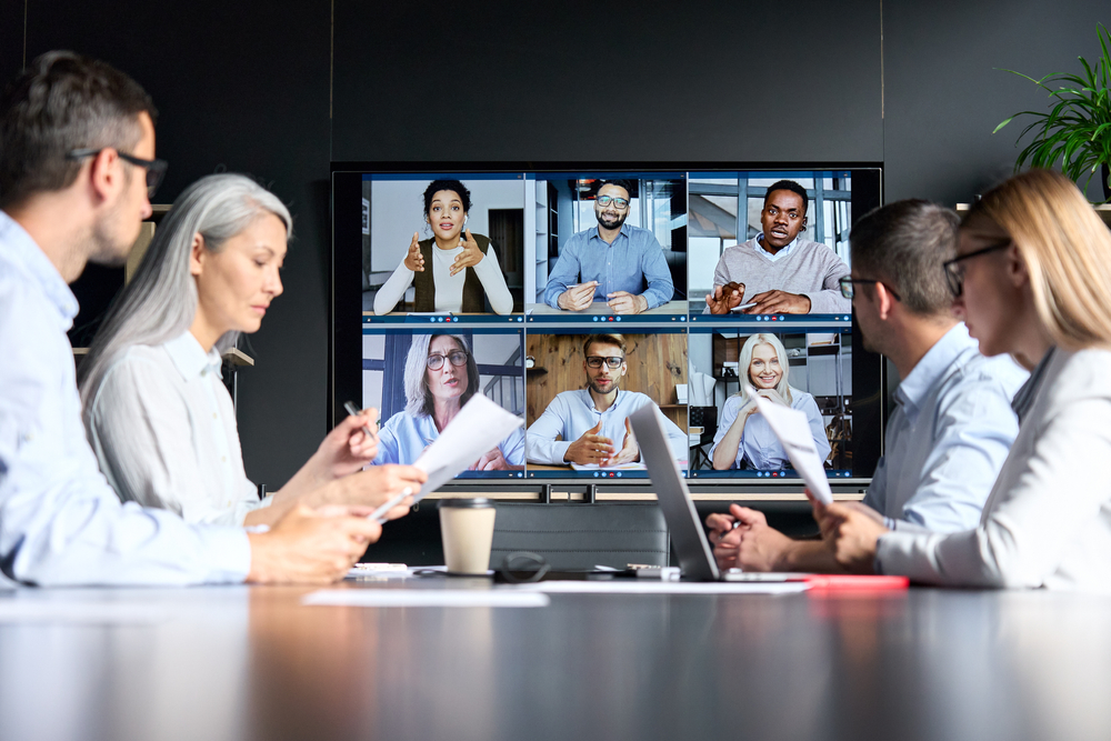 Equipo de colaboradores reunidos en sala de juntas tienen Videoconferencia con otros miembros que trabajan a distancia. 